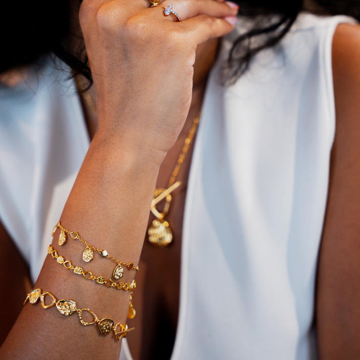 Close-up of a person wearing gold jewelry including bracelets and a necklace.