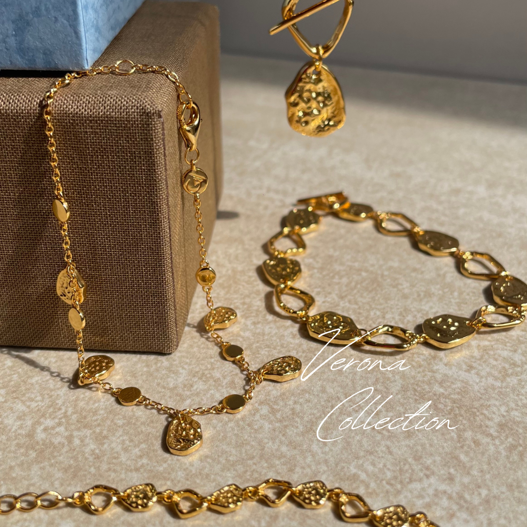 Gold jewelry set including necklace and bracelet on a textured surface with 'Verona Collection' branding.